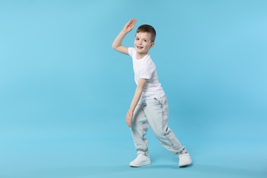 Photo of Happy little boy dancing on light blue background. Space for text