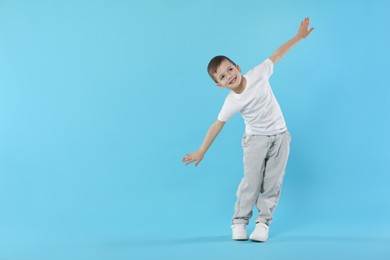 Photo of Happy little boy dancing on light blue background. Space for text