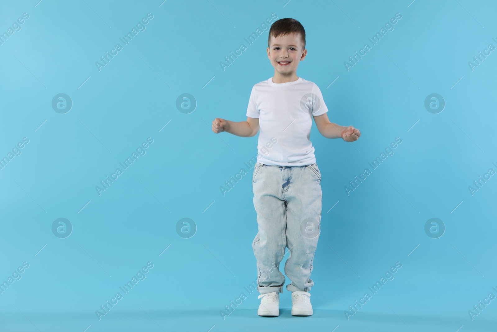 Happy little boy dancing on light blue background. Space for text Photo of Happy little boy dancing on light blue background. Space for text