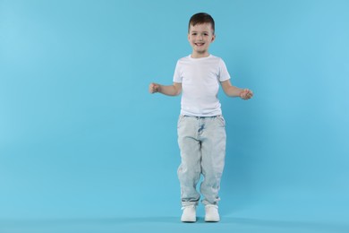 Photo of Happy little boy dancing on light blue background. Space for text