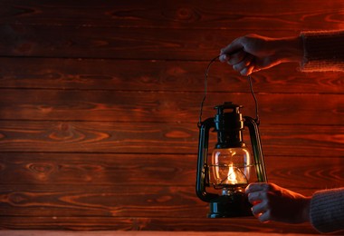 Photo of Woman holding vintage kerosene lantern near wooden wall, closeup. Space for text
