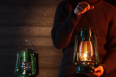 Photo of Man holding vintage kerosene lantern near wooden wall, closeup. Space for text