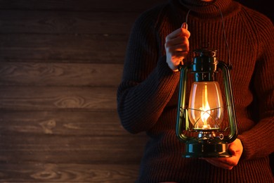 Photo of Man holding vintage kerosene lantern near wooden wall, closeup. Space for text