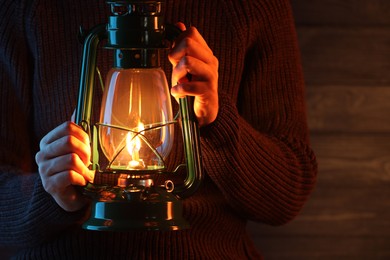 Photo of Man holding vintage kerosene lantern near wooden wall, closeup. Space for text