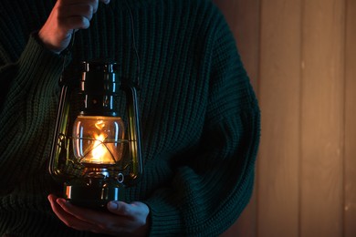 Photo of Woman holding vintage kerosene lantern near wooden wall, closeup. Space for text