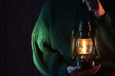 Photo of Woman holding vintage kerosene lantern near wooden wall, closeup. Space for text