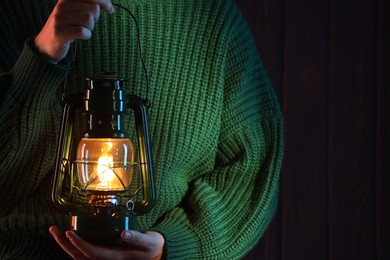 Photo of Woman holding vintage kerosene lantern near wooden wall, closeup. Space for text