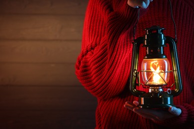 Photo of Woman holding vintage kerosene lantern near wooden wall, closeup. Space for text