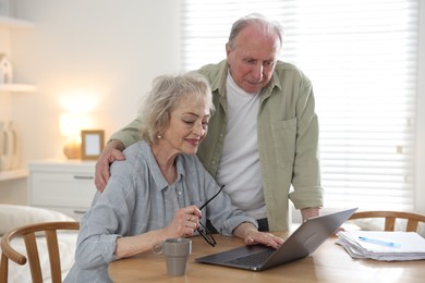 Photo of Lovely senior couple watching something on laptop at table indoors