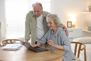 Photo of Lovely senior couple watching something on laptop at table indoors