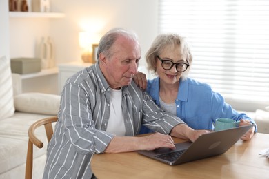 Photo of Lovely senior couple watching something on laptop at table indoors