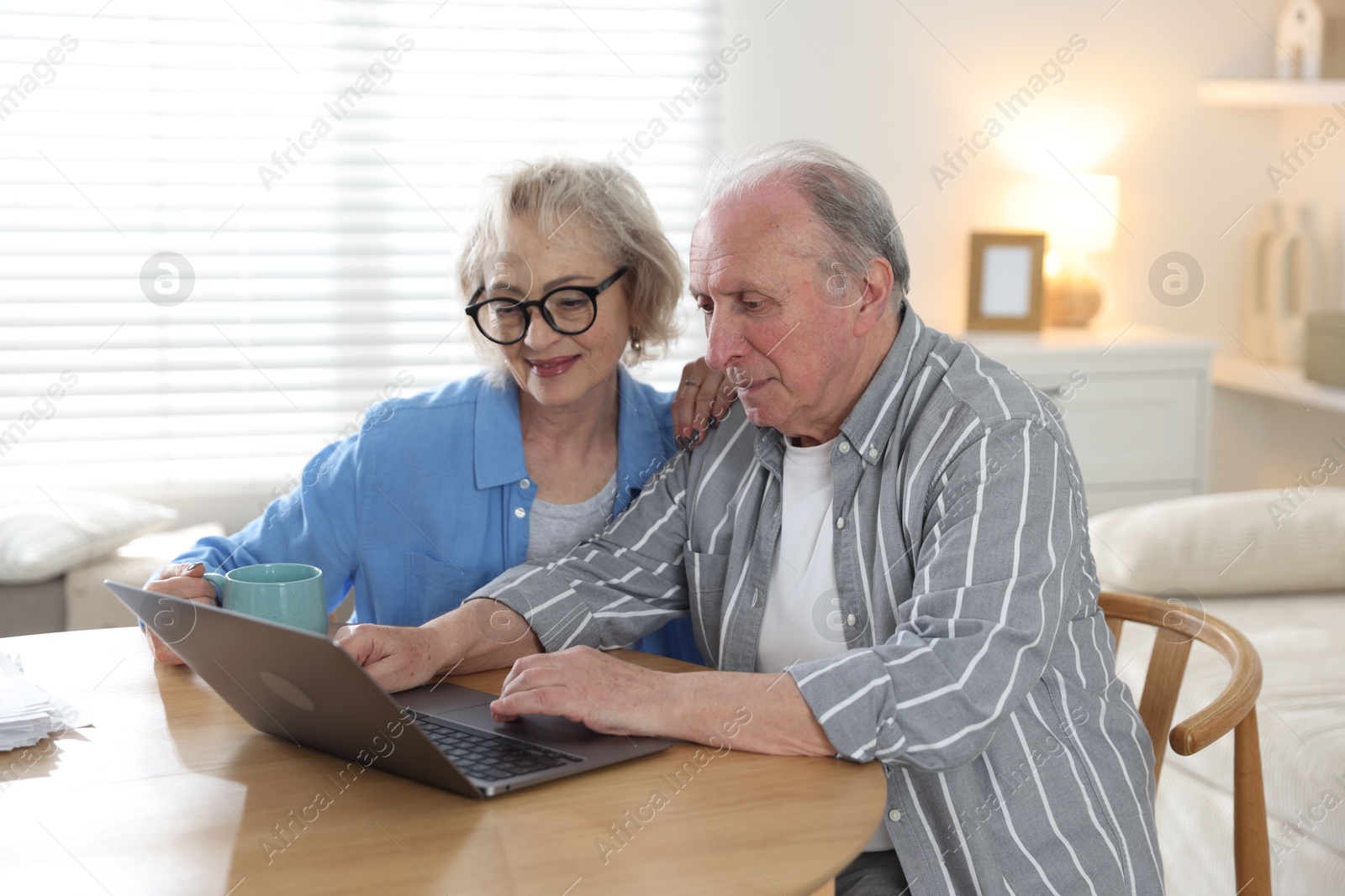 Lovely senior couple watching something on laptop at table indoors Photo of Lovely senior couple watching something on laptop at table indoors