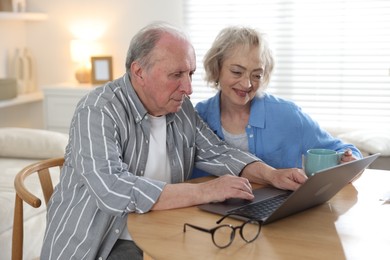 Photo of Lovely senior couple watching something on laptop at table indoors