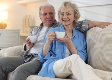 Photo of Lovely senior couple enjoying hot drinks on sofa at home