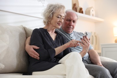 Photo of Lovely senior couple watching something on smartphone at home