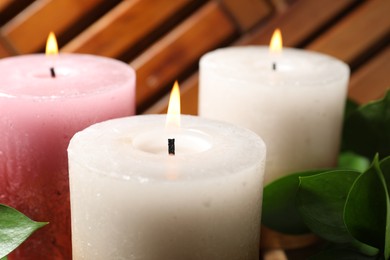 Photo of Burning candles and green leaves on table, closeup