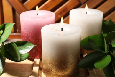 Photo of Burning candles and green leaves on wooden tray, closeup