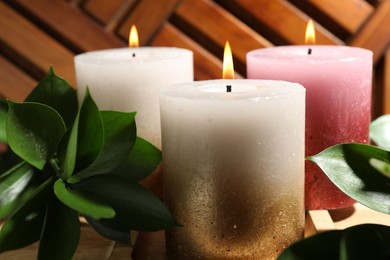 Photo of Burning candles and green leaves on wooden tray, closeup