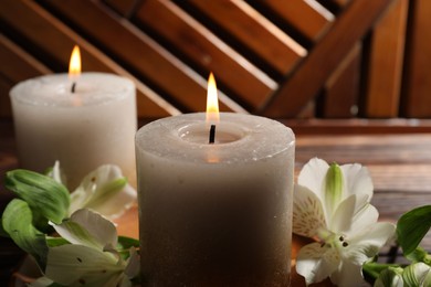 Photo of Burning candles and lily flowers on wooden table, closeup