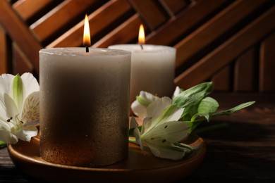Photo of Burning candles and lily flowers on wooden table, closeup
