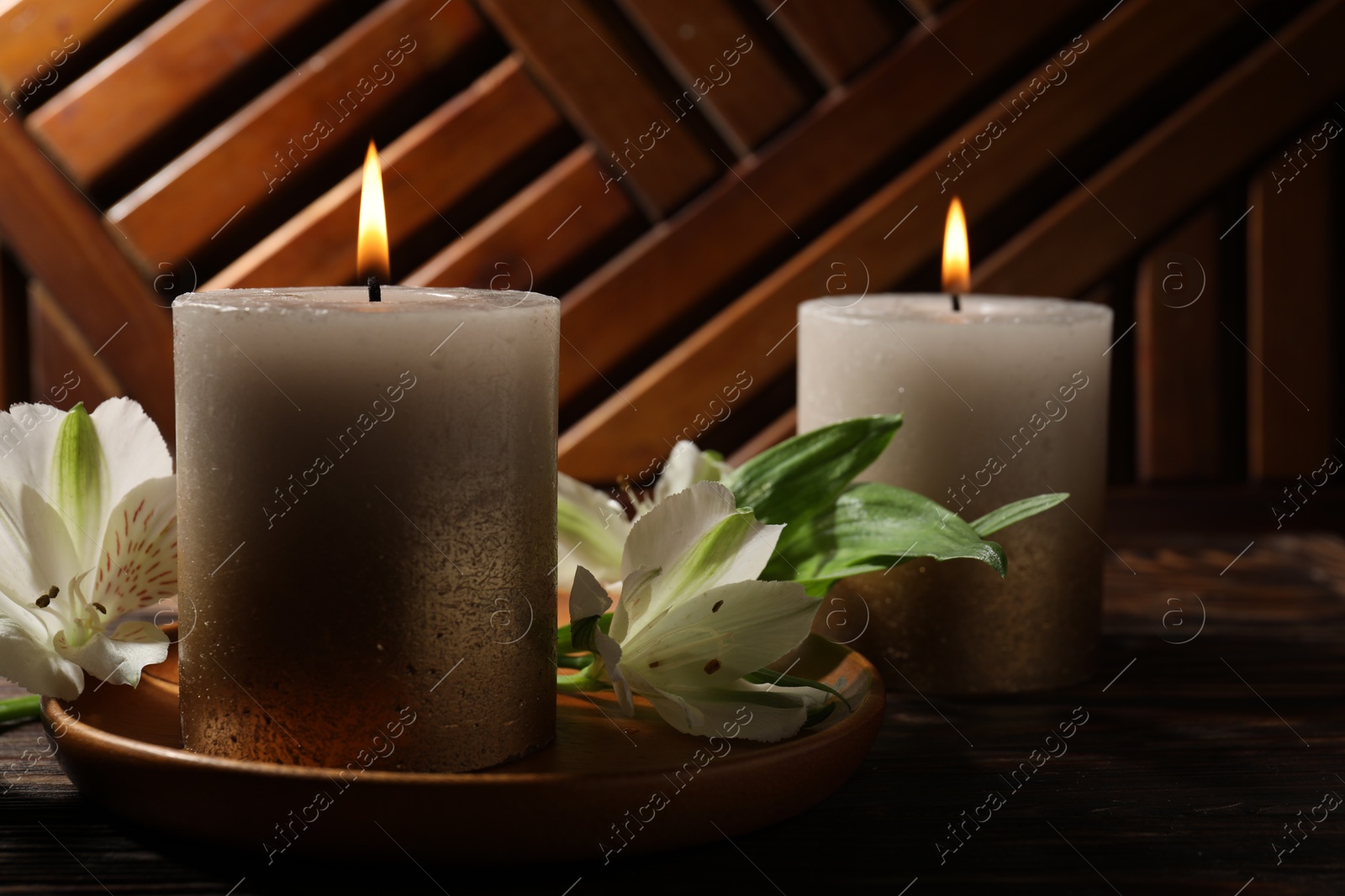 Photo of Burning candles and lily flowers on wooden table, closeup