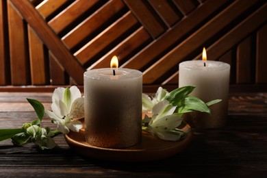 Photo of Burning candles and lily flowers on wooden table, closeup
