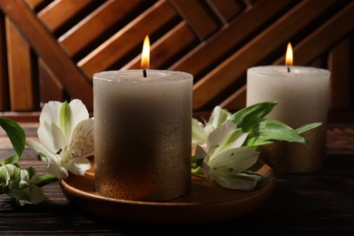 Photo of Burning candles and lily flowers on wooden table, closeup