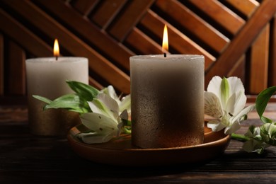 Photo of Burning candles and lily flowers on wooden table, closeup