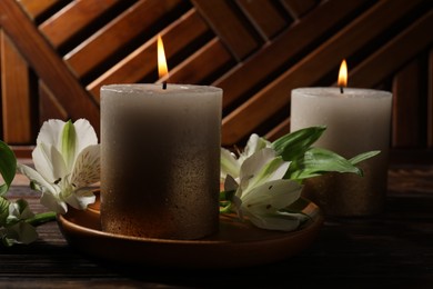 Photo of Burning candles and lily flowers on wooden table, closeup