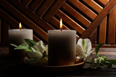 Photo of Burning candles and lily flowers on wooden table, closeup