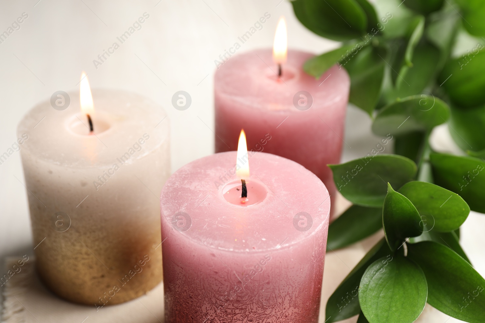 Burning candles and green leaves on white table, closeup Photo of Burning candles and green leaves on white table, closeup