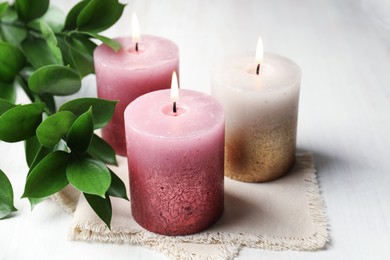 Photo of Burning candles and green leaves on white table, closeup