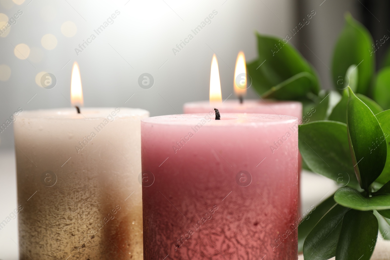 Burning candles and green leaves on table against blurred lights, closeup Photo of Burning candles and green leaves on table against blurred lights, closeup