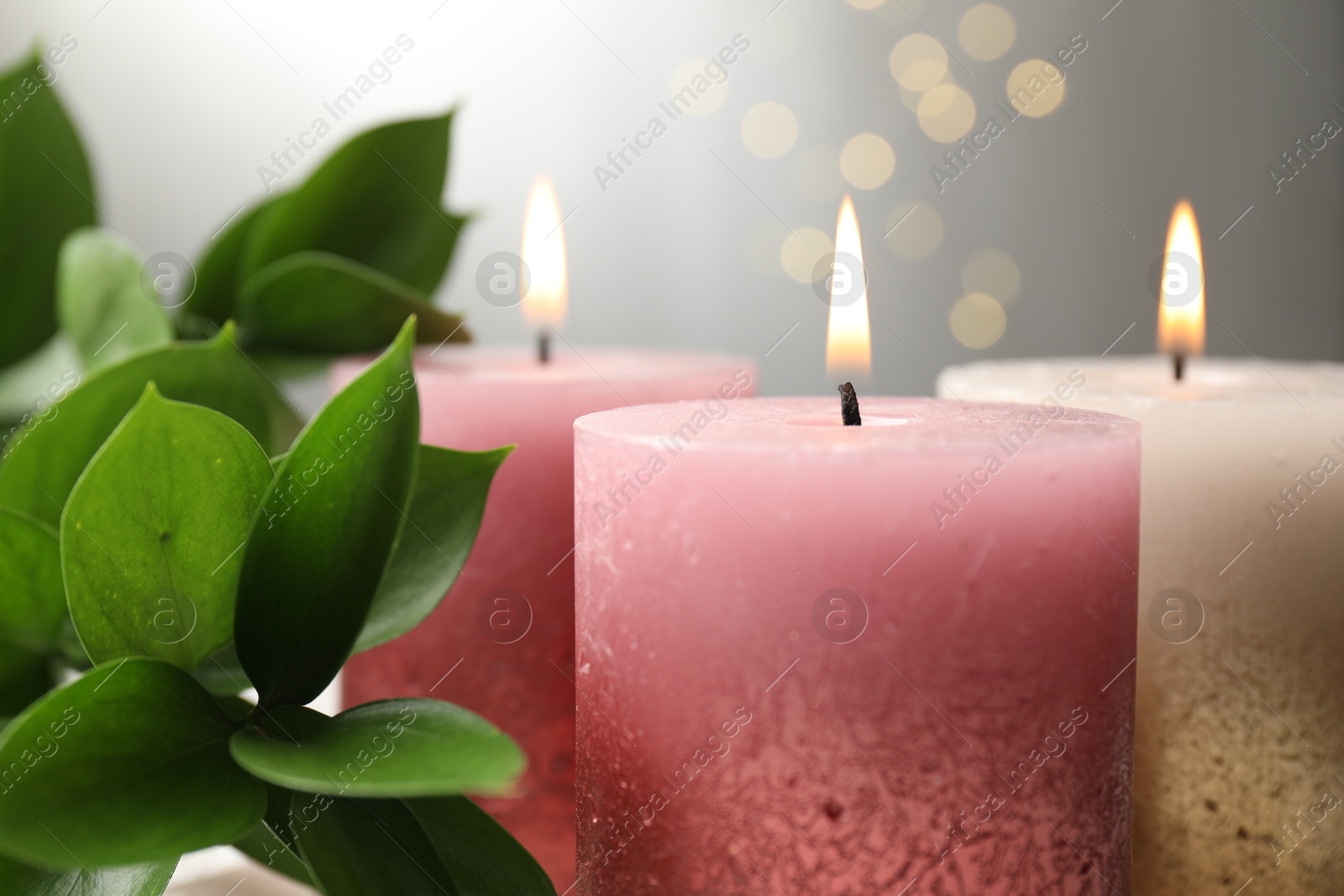 Burning candles and green leaves on table against blurred lights, closeup Photo of Burning candles and green leaves on table against blurred lights, closeup