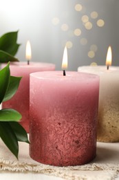 Photo of Burning candles and green leaves on white table, closeup