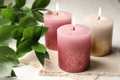 Photo of Burning candles and green leaves on white table, closeup
