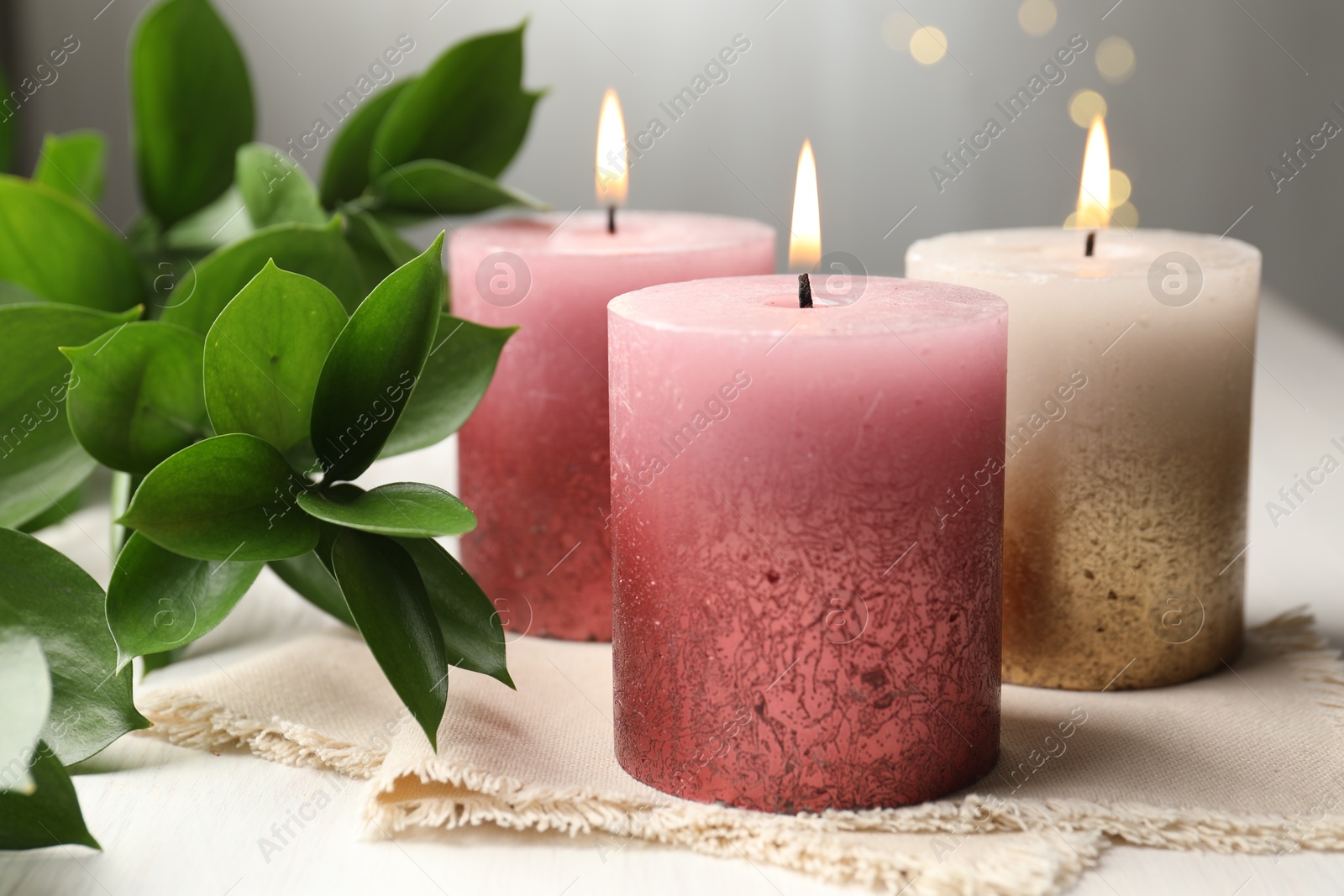 Burning candles and green leaves on white table against blurred lights, closeup Photo of Burning candles and green leaves on white table against blurred lights, closeup