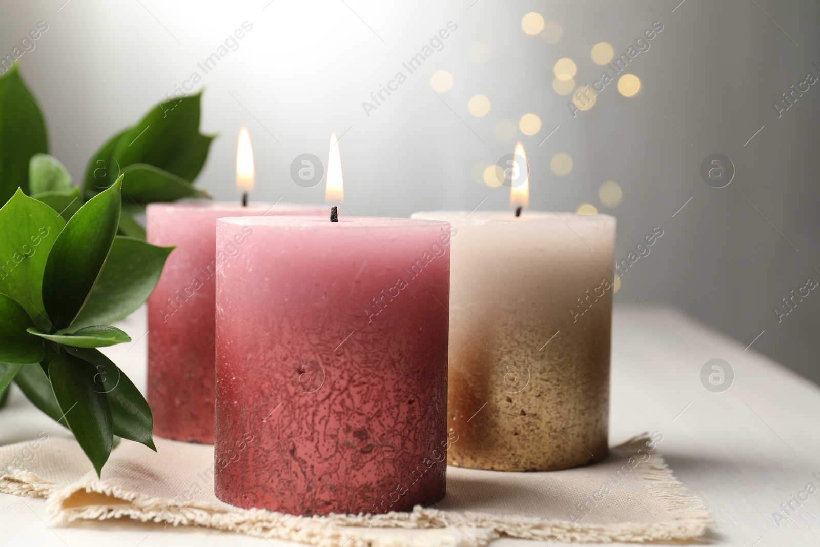 Burning candles and green leaves on white table against blurred lights, closeup Photo of Burning candles and green leaves on white table against blurred lights, closeup