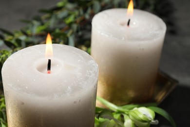 Photo of Burning candles and green leaves on table, closeup