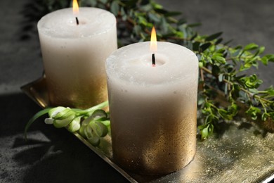 Photo of Burning candles and green leaves on black table, closeup