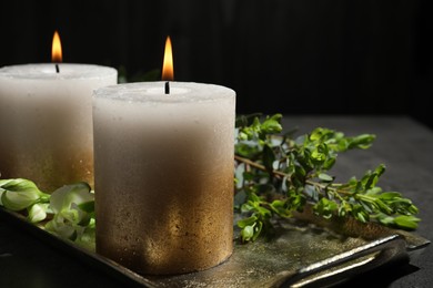 Photo of Burning candles and green leaves on black table, closeup