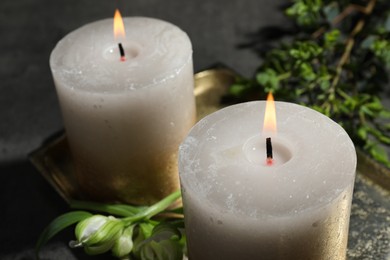 Photo of Burning candles and green leaves on black table, closeup