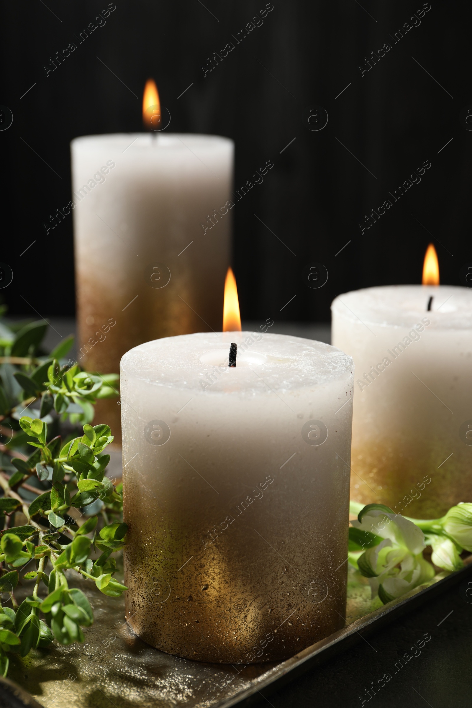 Burning candles and green leaves on black table, closeup Photo of Burning candles and green leaves on black table, closeup