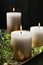 Photo of Burning candles and green leaves on black table, closeup