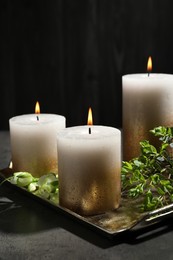 Photo of Burning candles and green leaves on black table, closeup