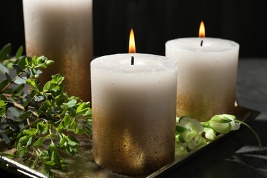 Photo of Burning candles and green leaves on black table, closeup