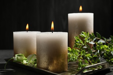 Photo of Burning candles and green leaves on black table, closeup