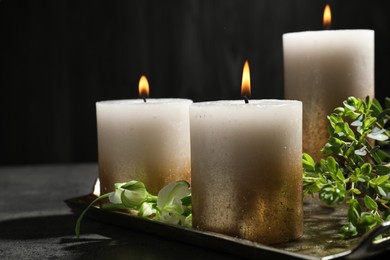 Photo of Burning candles and green leaves on black table, closeup