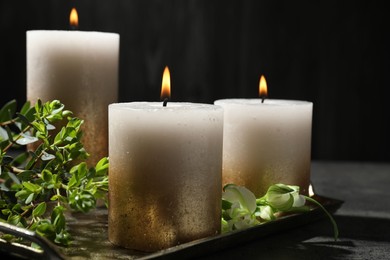 Photo of Burning candles and green leaves on black table, closeup