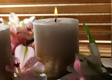 Photo of Burning candles and lily flowers on table, closeup